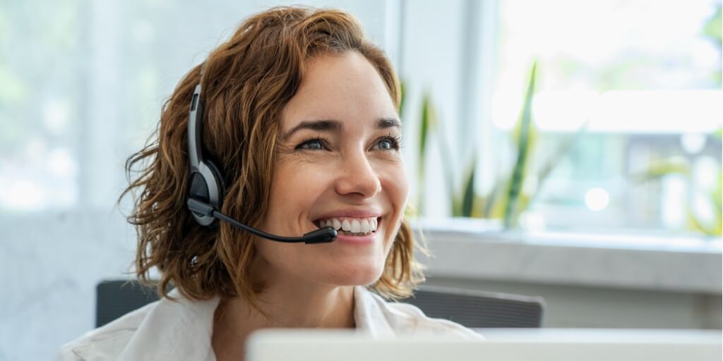 Primer plano de una mujer madura y sonriente atendiendo al cliente con auriculares en la oficina.