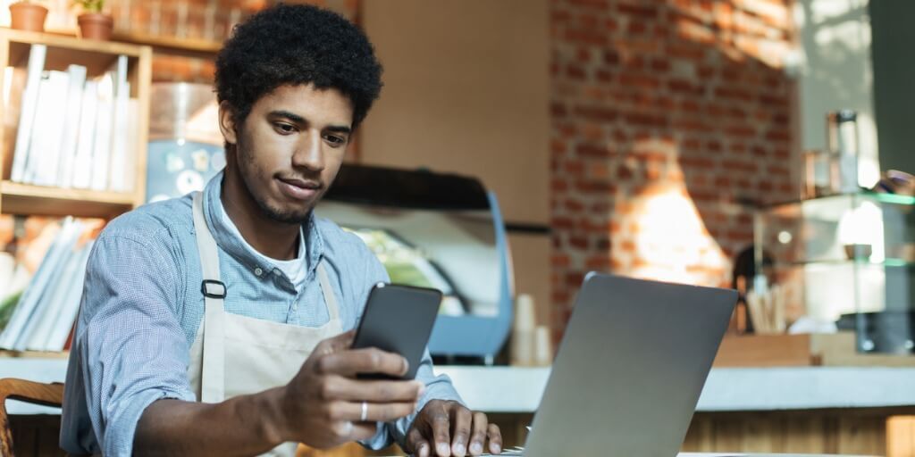 Un hombre con delantal accede al software de atención al cliente desde su smartphone y su ordenador portátil.