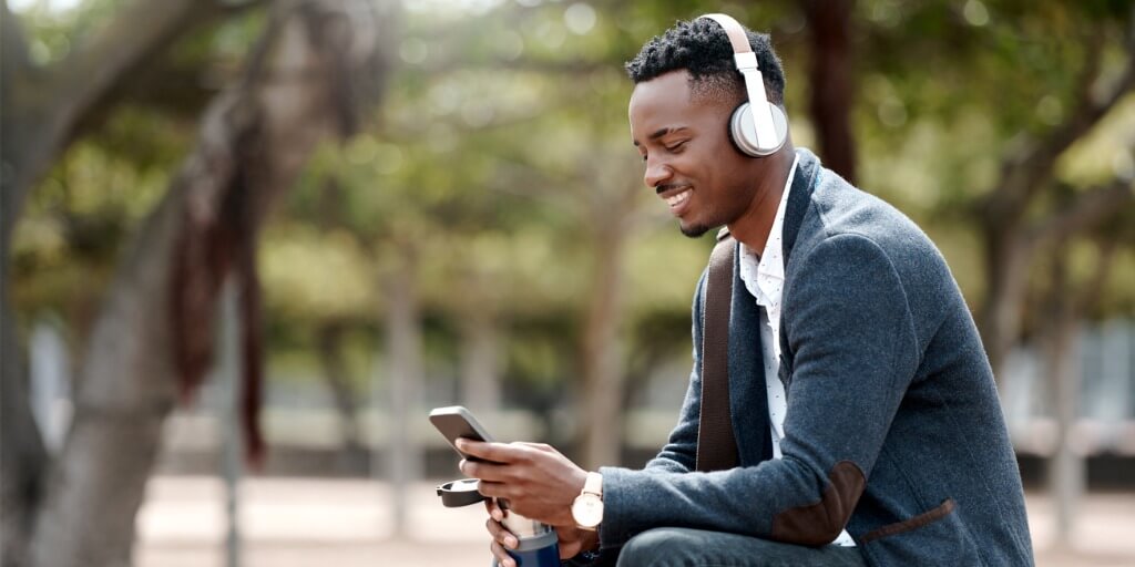 Un hombre de negocios se sienta en un parque a escuchar podcasts sobre la experiencia del cliente en su teléfono