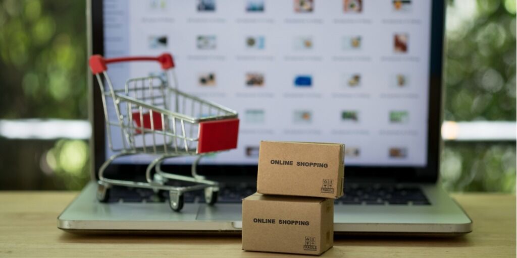 Boîtes en carton miniatures avec chariot de supermarché et ordinateur portable en arrière-plan. Concept d'achat en ligne