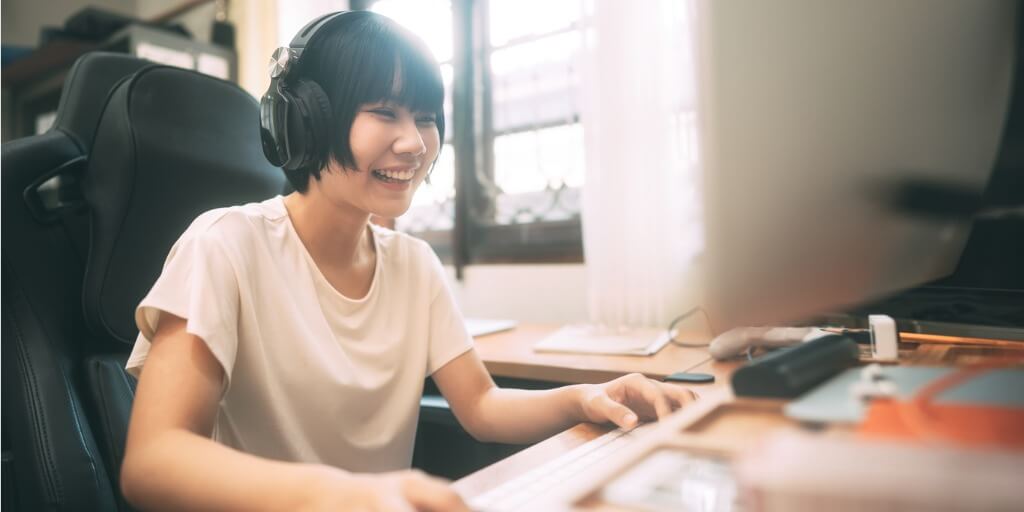 Happy young adult woman stay-at-home concept. She wears headphone using computer communication via internet online technology showing benefits of live chat for ecommerce